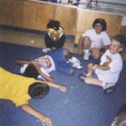 The photograph shows children dramatizing dying dinosaurs and a sun.