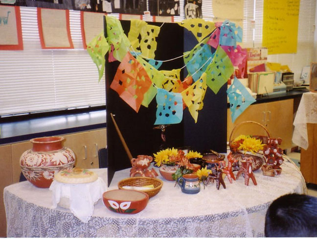The photo shows the children's altar displaying papel picado and artifacts related to El día de los muertos